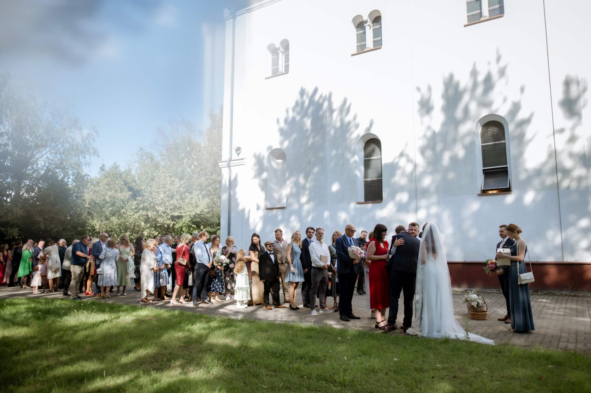 goście składają życzenia parze młodej po ślubie pod kościołem